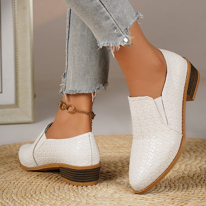 White heeled loafers with pointed toe, one foot forward, side view