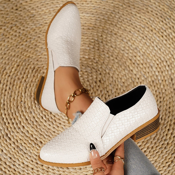 White woven look heeled loafers with pointed toe, shown on a woven mat