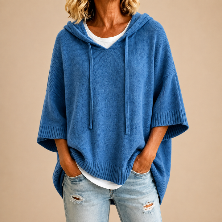 Cobalt blue knit poncho sweater with hood and drawstrings, hands in pockets