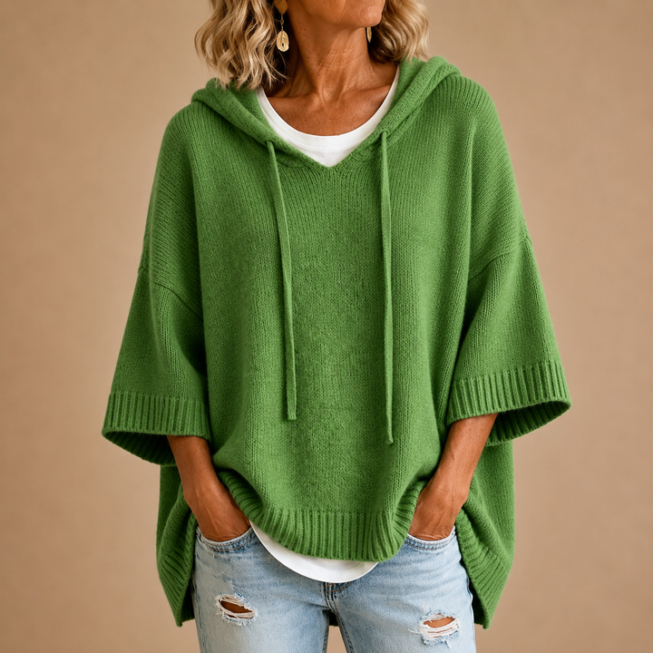 Green hooded poncho sweater with a relaxed fit, worn over a white tee