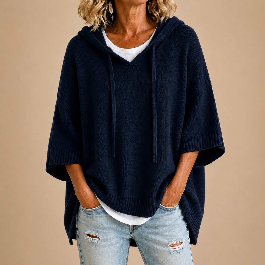 Navy hooded poncho sweater layered over a white top and light jeans
