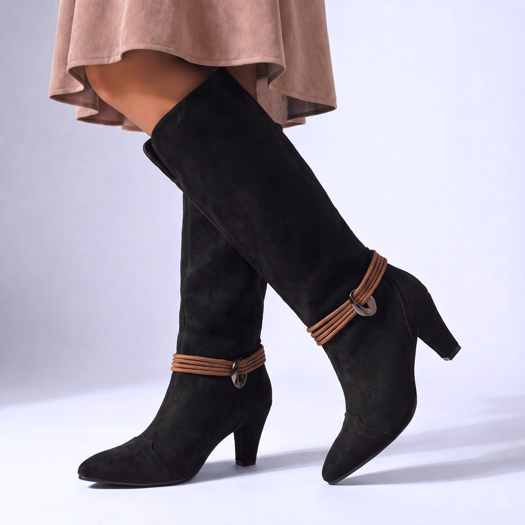 Black suede-look knee high boots on a model, tall shaft with ankle strap and heel