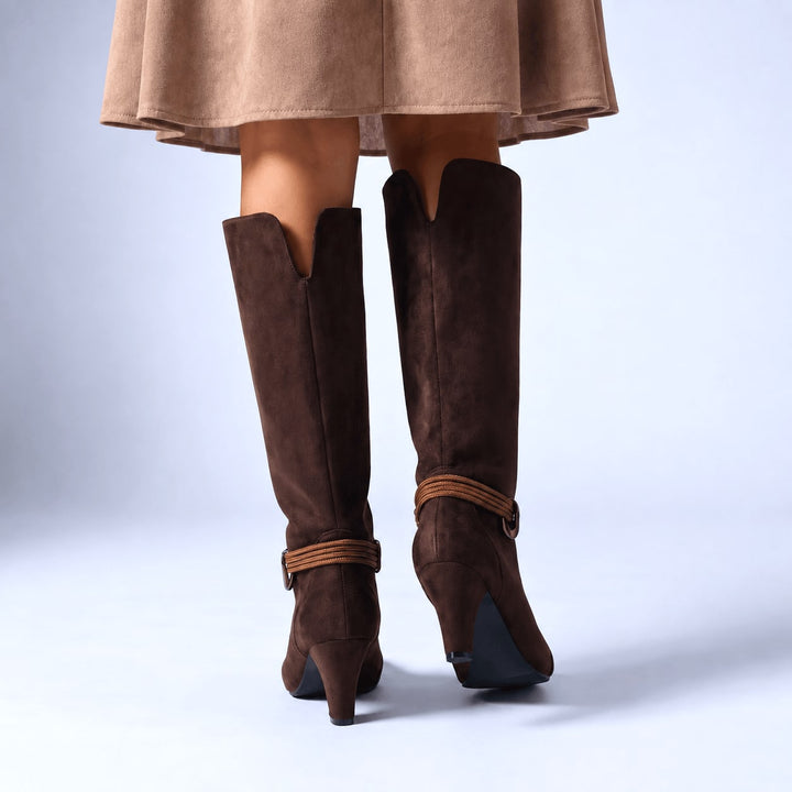 Front view of chocolate knee high boots worn with a beige skirt, ankle straps visible