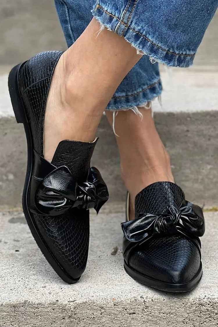 Black bow loafers worn on stone steps, perforated upper visible