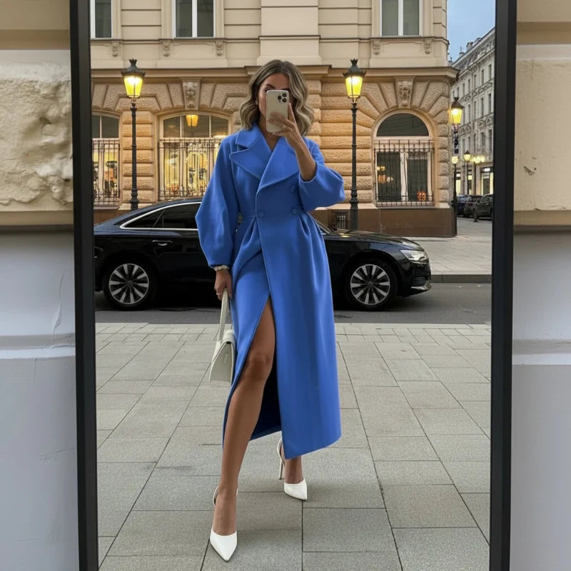 Woman in a blue long coat walking past a city street with a white bag