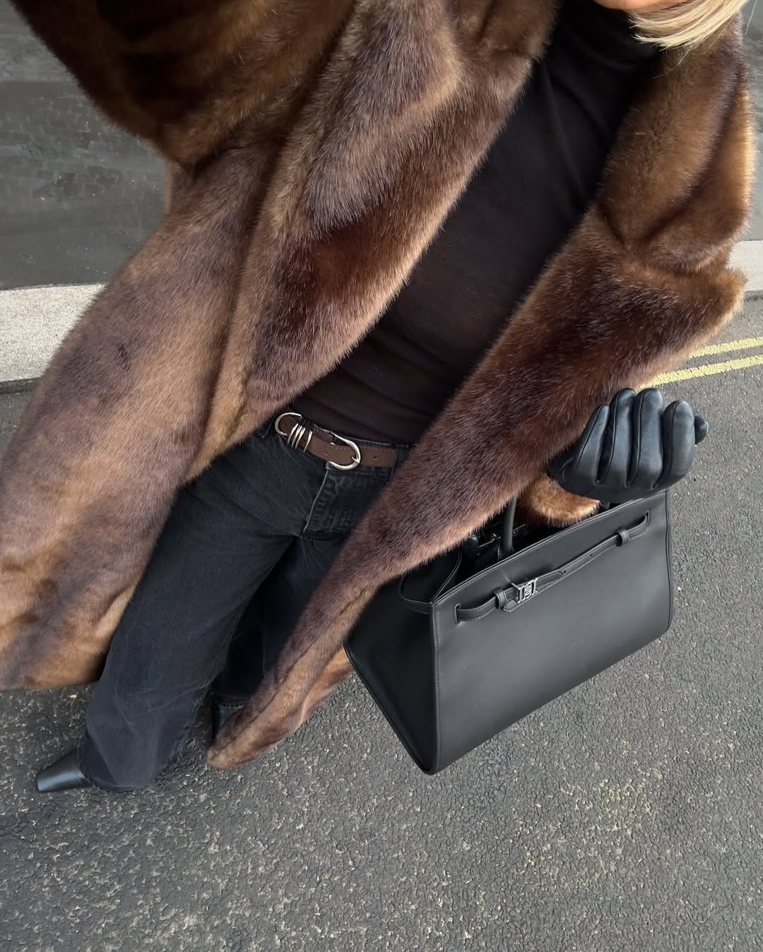 Close up of the dark brown faux fur coat sleeve and lapel with a black handbag