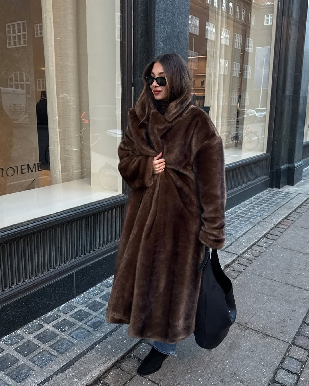 Front view of the dark brown maxi faux fur coat with a high collar on a street