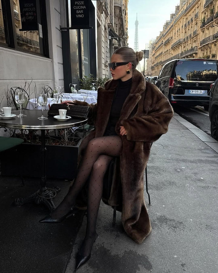 Seated model in the dark brown faux fur maxi coat at a street cafe
