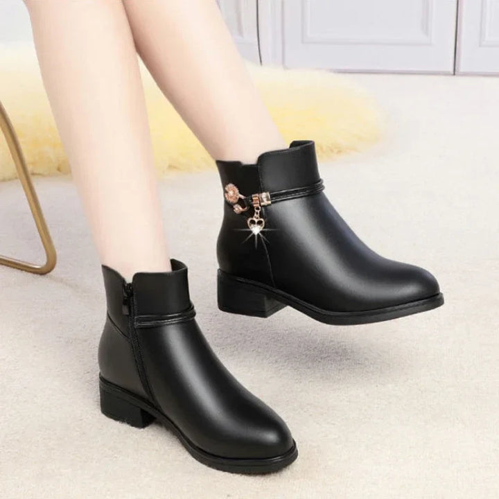 Black low heel ankle boots with gold charm worn with one foot lifted, bare legs