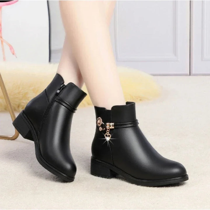 Black low heel ankle boots with gold charm worn with bare legs on a cream rug