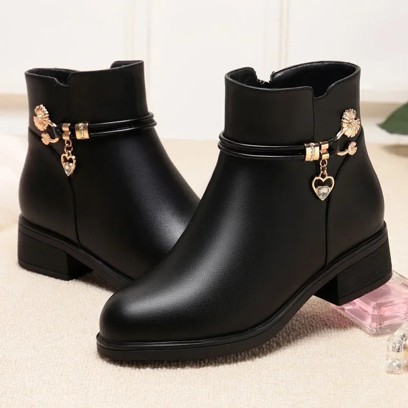 Women's low heel ankle boots in black with gold charm and side zip, pair on a light backdrop
