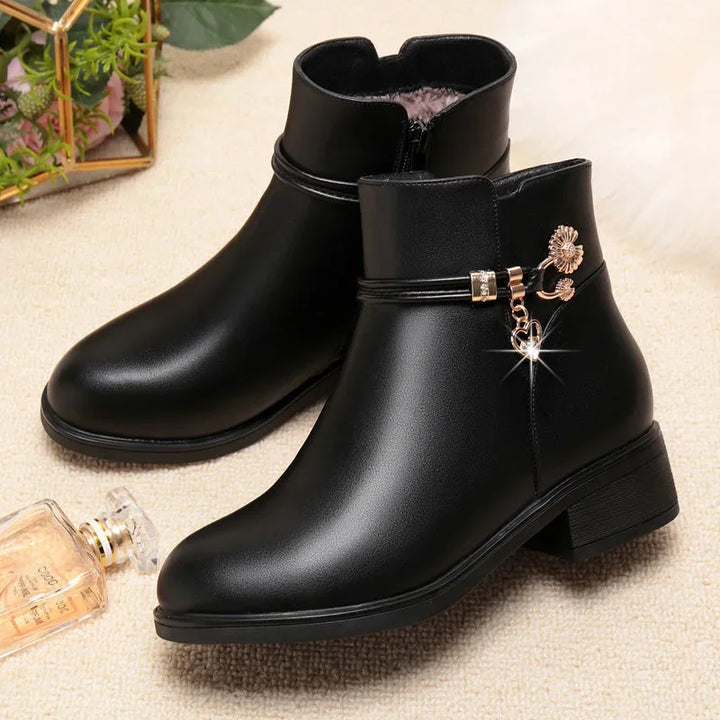 Black low heel ankle boots with gold charm detail and side zip on a green leaf backdrop