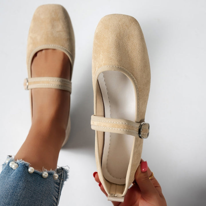 Overhead view of beige Mary Jane flats with buckle, held over pearl trim jeans