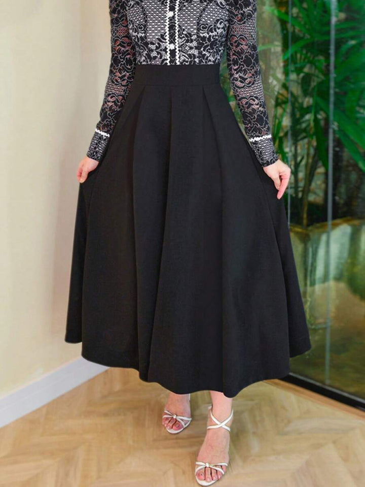 Black high waist maxi skirt flared at the hem, hand resting in a pocket