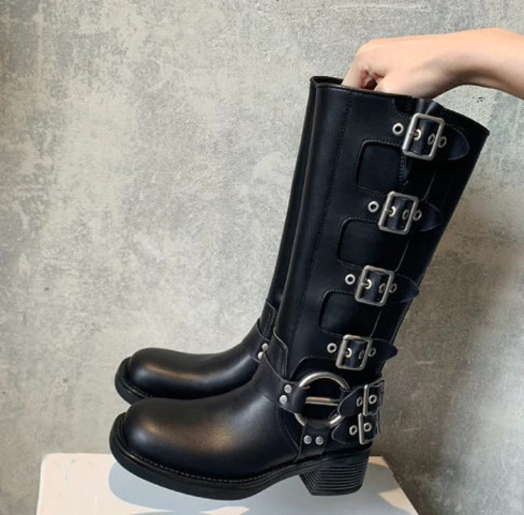 Black tall motorcycle boots with four buckle straps and ring hardware, front view
