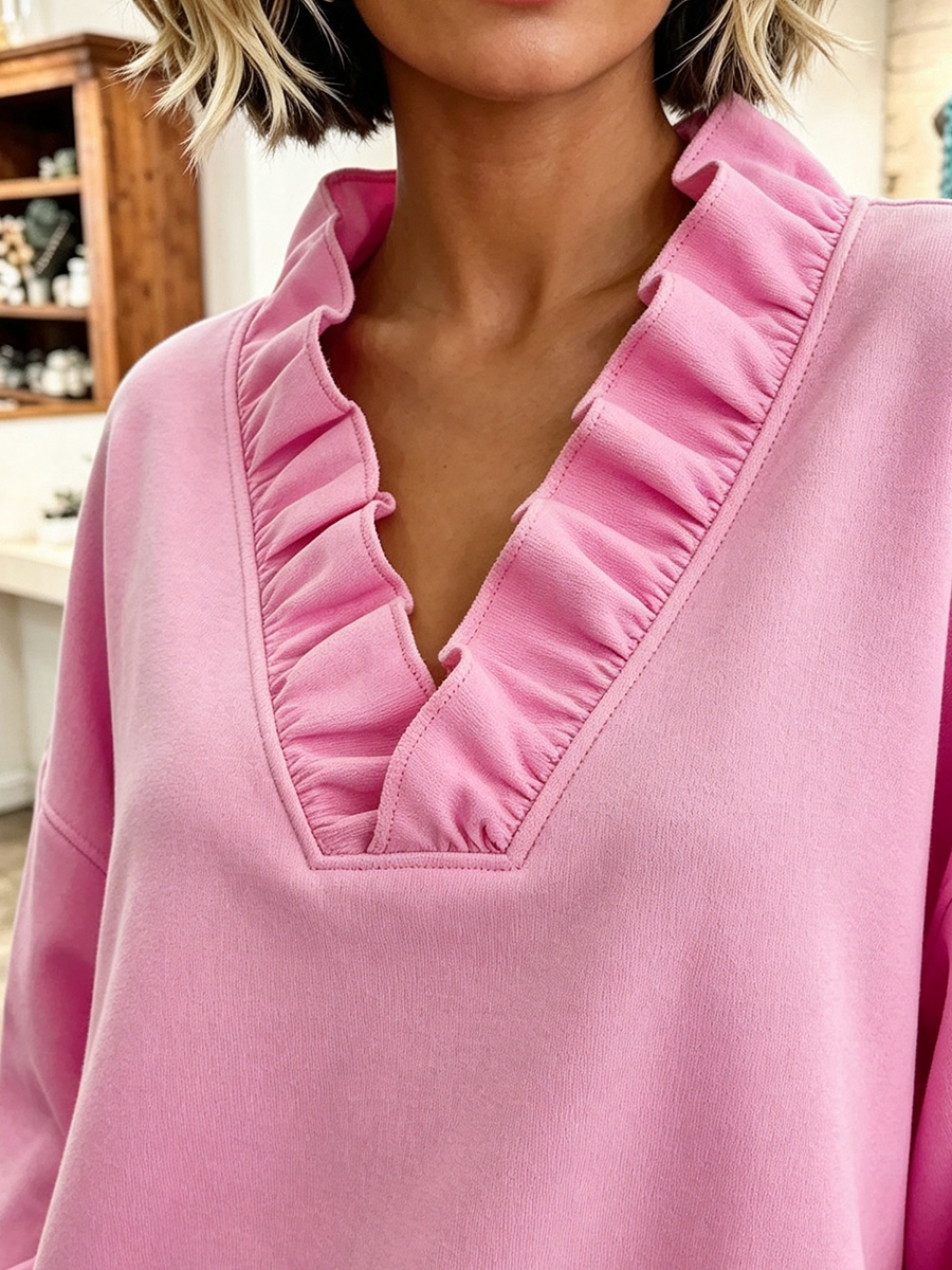 Close-up of the ruffle trim along the deep V-neck of the pink sweatshirt