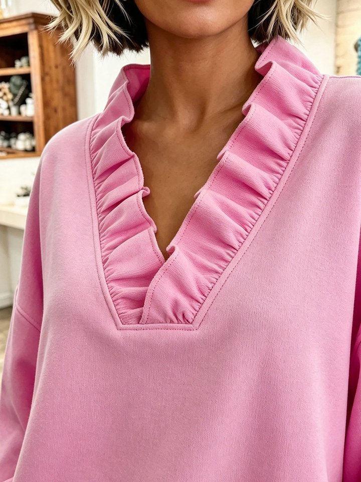 Close-up of the ruffle trim along the deep V-neck of the pink sweatshirt