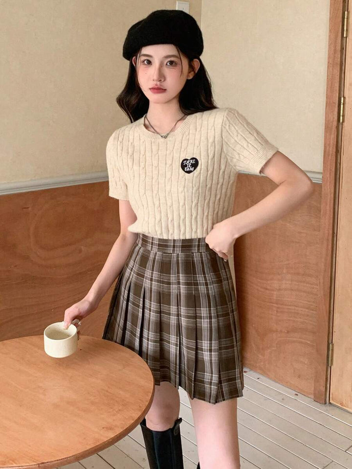 Model holding a cup in a brown pleated plaid skirt and beret