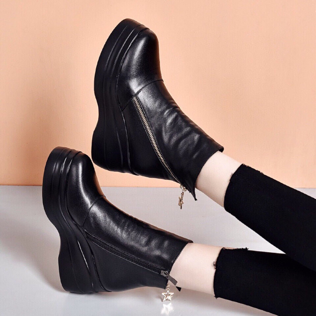 Black wedge platform booties worn with one foot raised, diagonal zip visible
