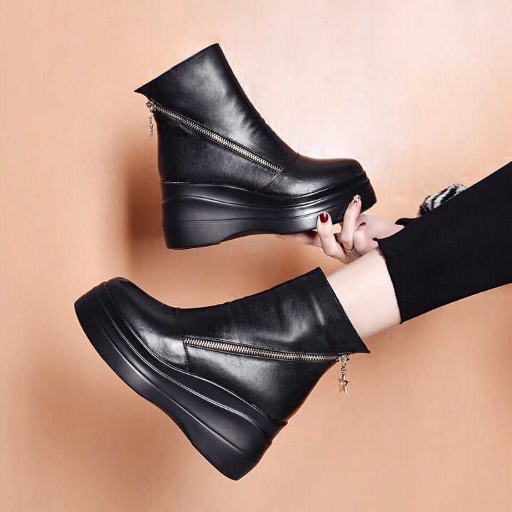 Pair of black platform wedge booties worn with black leggings, seen from above