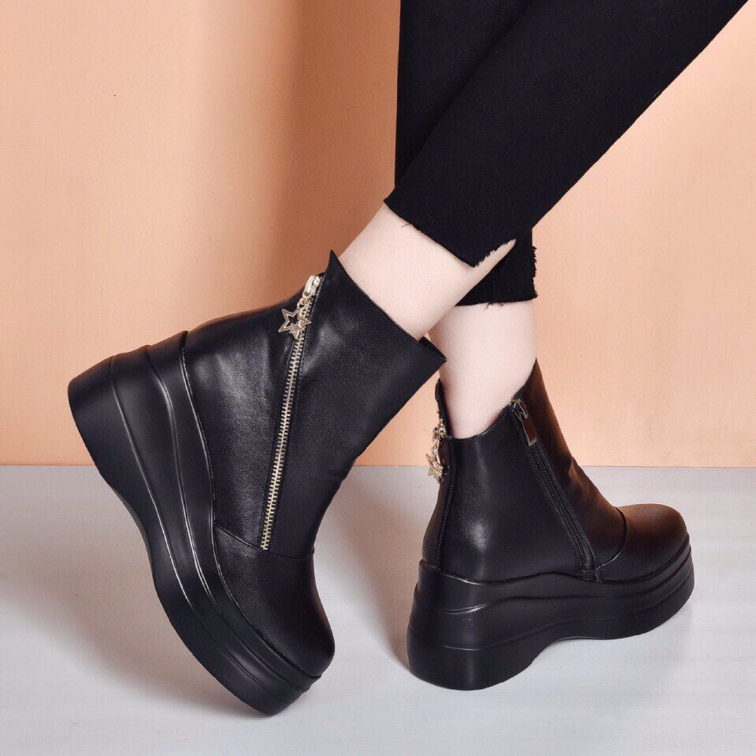 Side view of black wedge platform booties with diagonal zip against a peach background