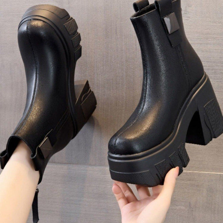 Black chunky lug sole ankle boot held in a hand showing the back tab