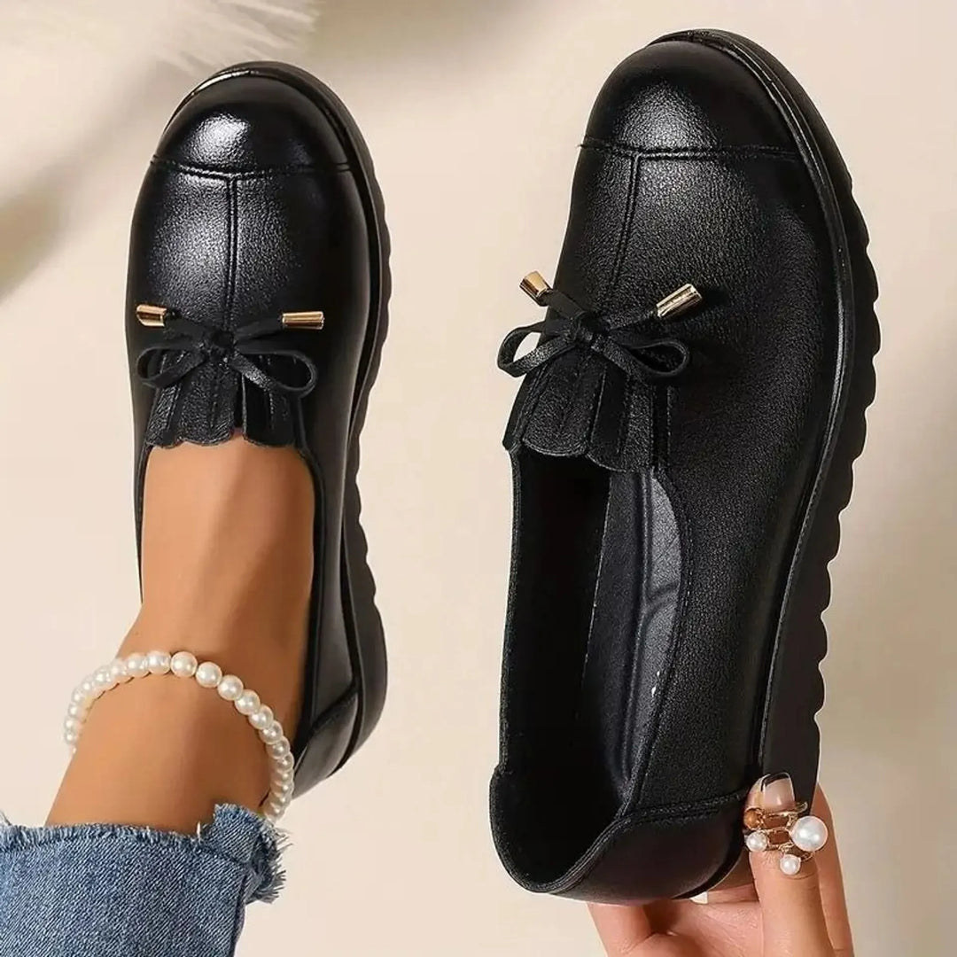 Women's platform loafers in black, round toe with bow and fringe, worn with pearl anklet