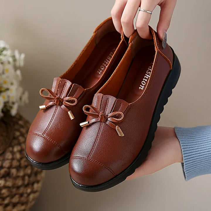 Pair of cognac loafers with fringe bow held up to show the thick sole
