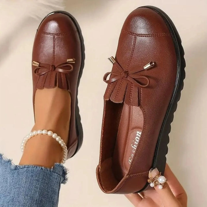 Cognac round toe platform loafers with bow and fringe, held in hand