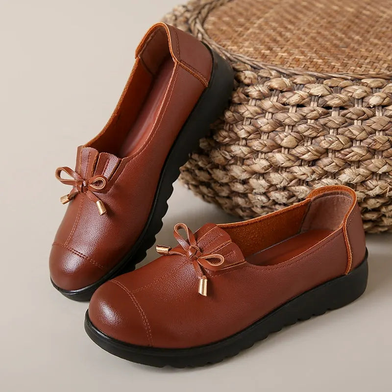 Cognac bow loafers resting on a woven basket, angled side view