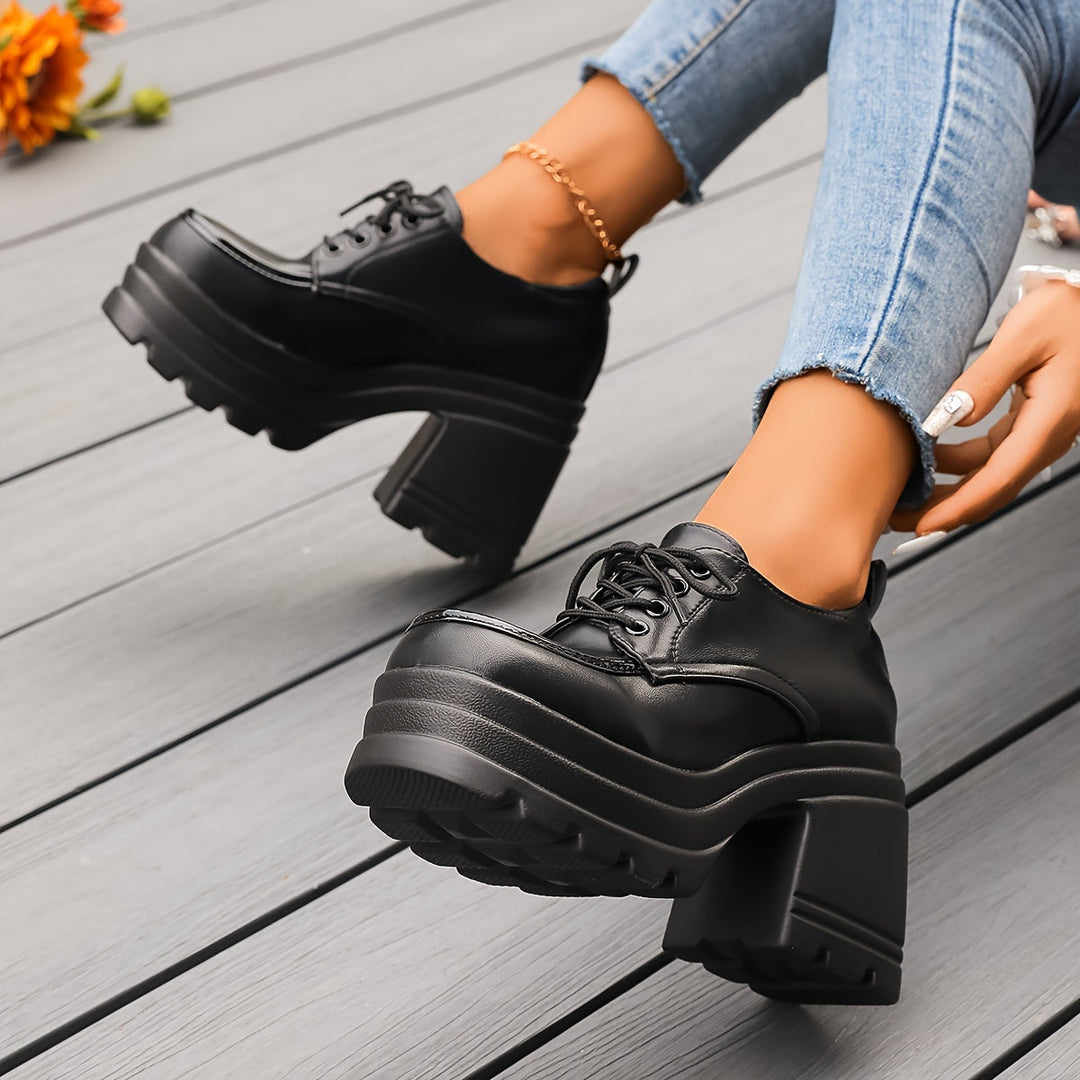 Black lace up platform Oxford shoe with chunky sole, one shoe lifted while worn