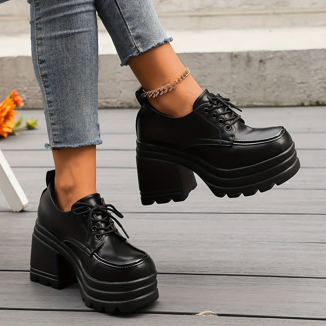Black chunky lace up platform Oxford shoes with block heel worn with jeans on a wooden deck