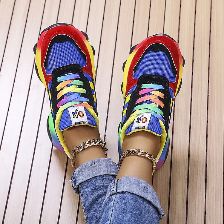 Top-down view of blue multi sneakers with rainbow laces and chain anklet