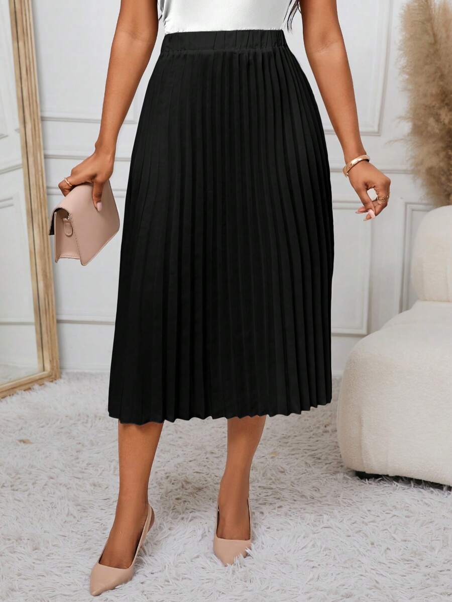 Black A-line pleated skirt styled with nude pumps and a clutch, angled view