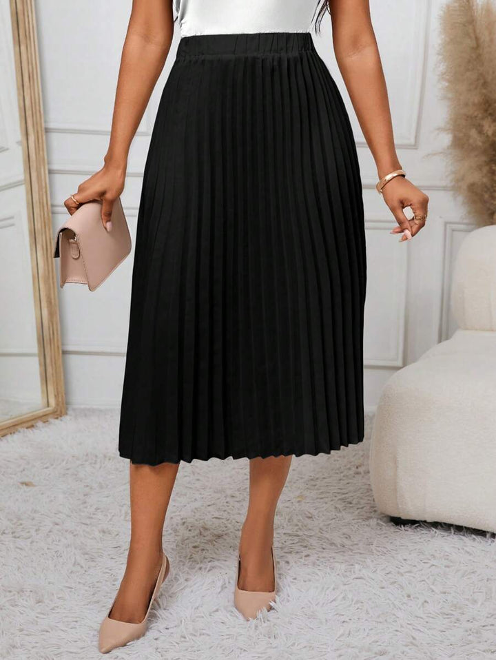 Black A-line pleated skirt styled with nude pumps and a clutch, angled view
