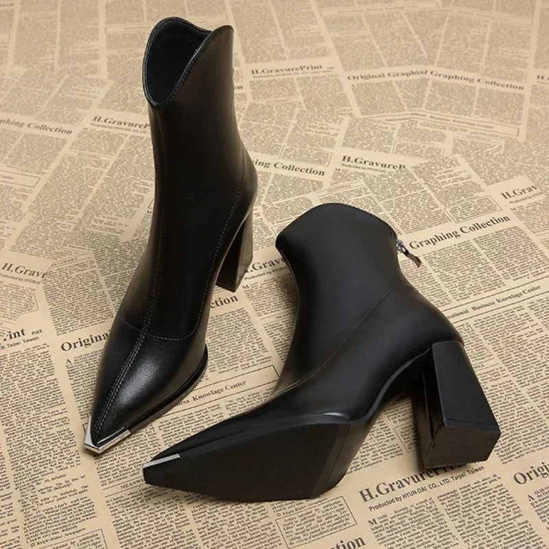 Women's pointed toe ankle boots in black with block heel and metal tip, pair on a newspaper print surface