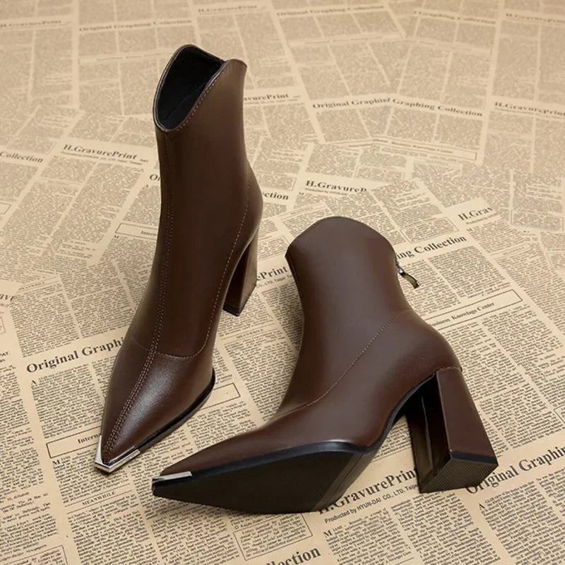 Brown pointed toe ankle boots with block heel and silver toe tip on a newspaper print surface