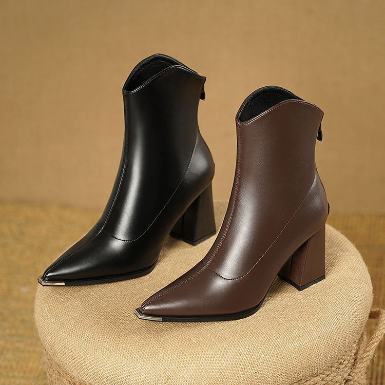 Black and brown pointed toe block heel ankle boots side by side on a woven stool