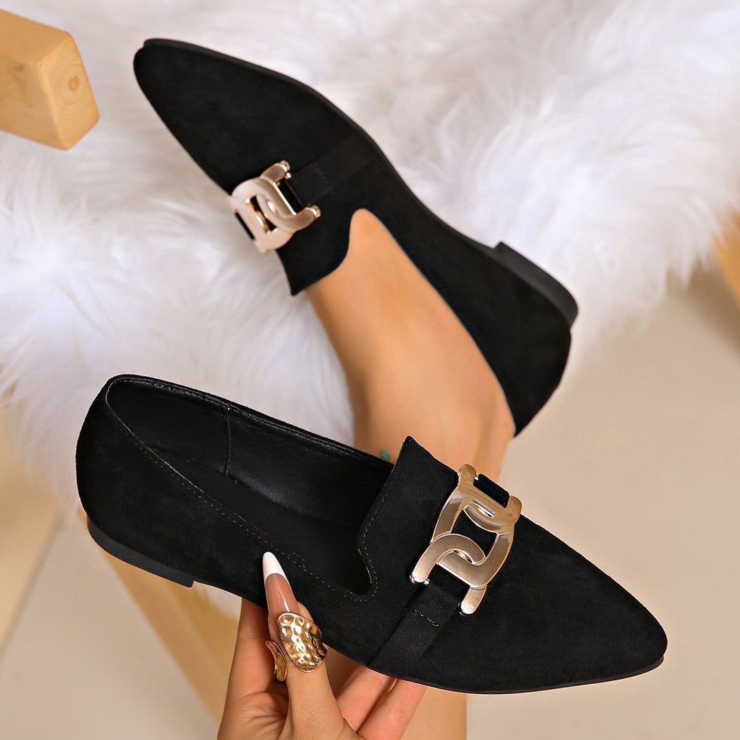 Black pointed toe loafers with a gold chain detail shown on foot
