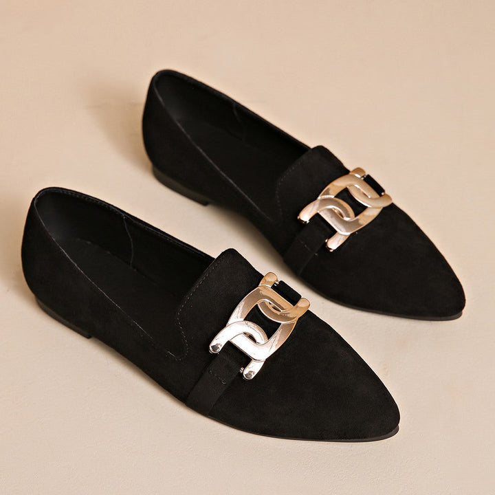 Pair of black pointed toe loafers with metal chain buckles on a beige surface