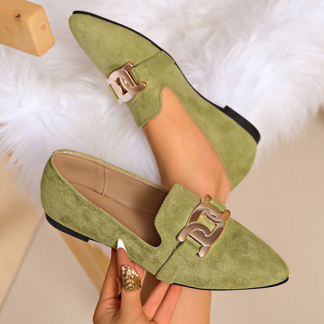 Olive suede look loafers with a chain buckle, held in hand on a fluffy rug