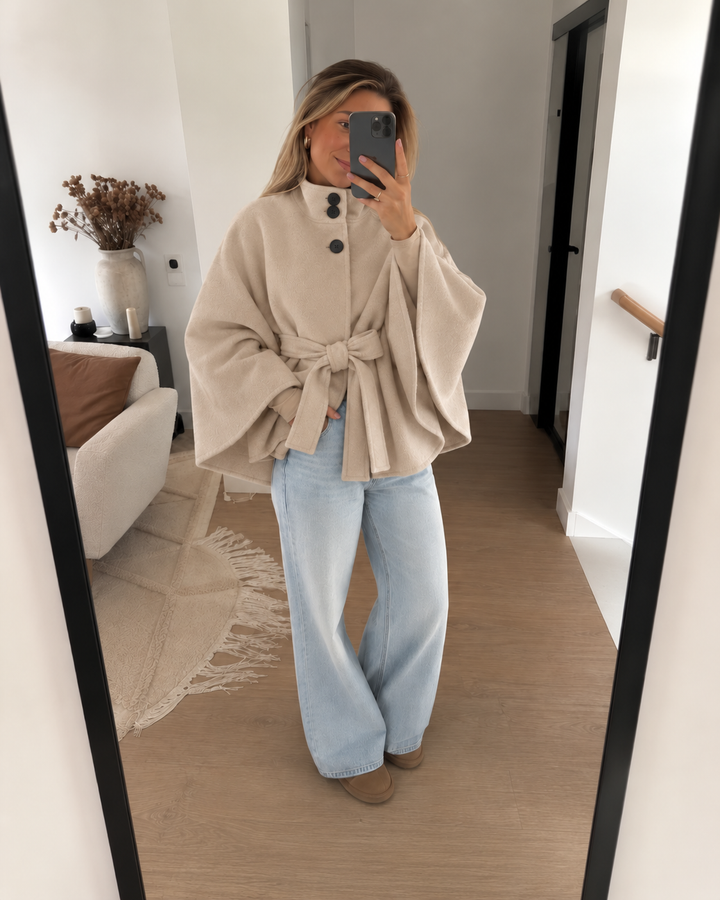 Woman taking a mirror selfie in a beige belted poncho coat and wide leg jeans