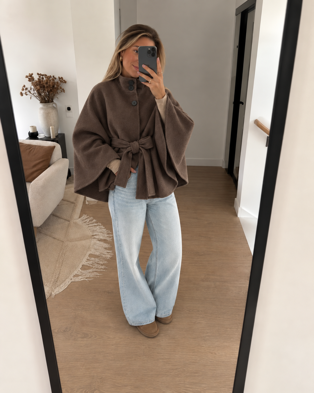 Brown belted cape coat worn with wide leg jeans in an indoor mirror selfie