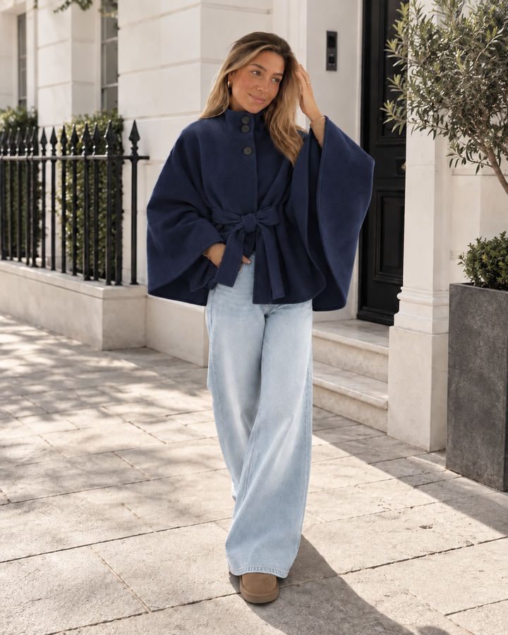 Navy belted poncho coat styled with light blue wide leg jeans on a sunny street