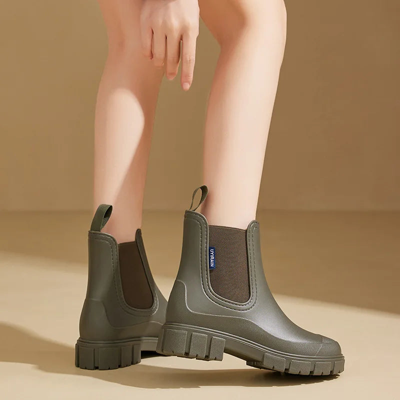 Olive Chelsea rain boots worn on a tan studio backdrop, front angle