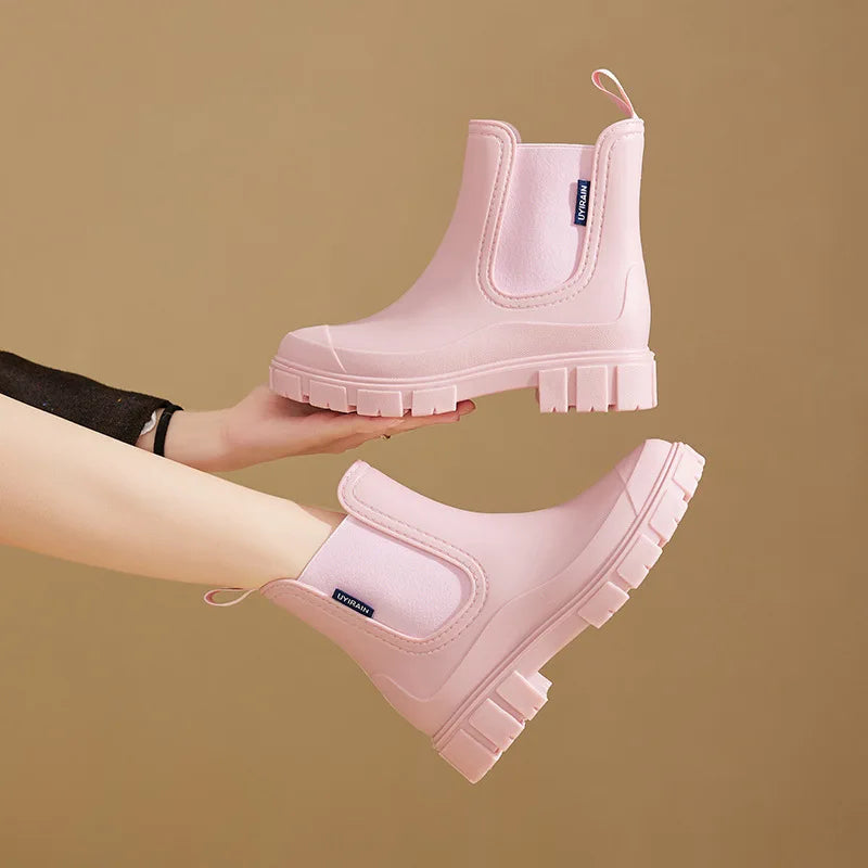 Pink Chelsea ankle rain boots held in hand, one tilted to show the tread