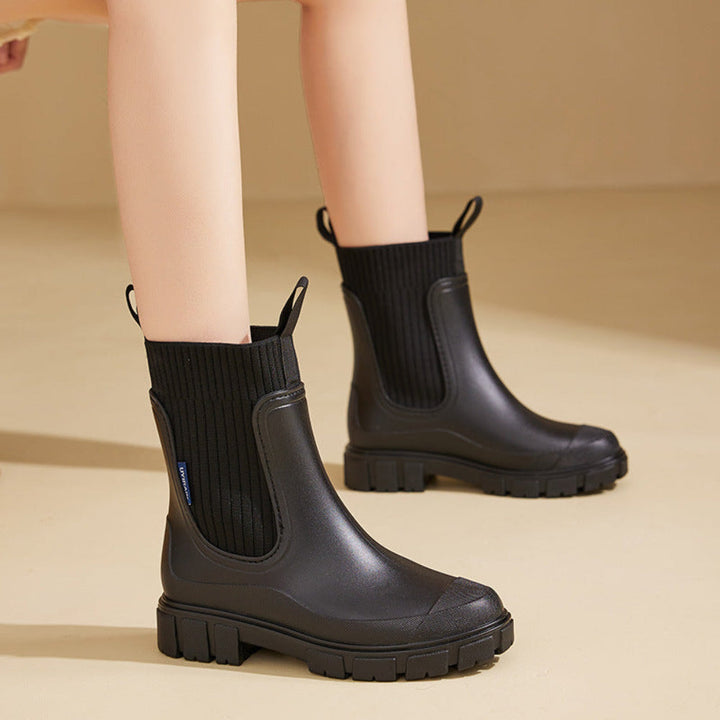 Black chelsea rain boots with knit collar worn with bare legs, standing pose