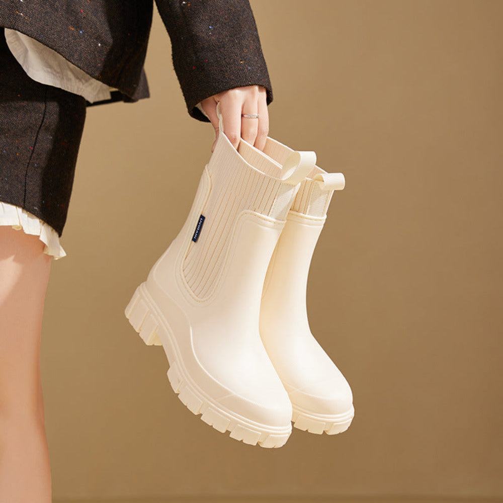 Cream rain boot held by a model, showing the chunky lug sole