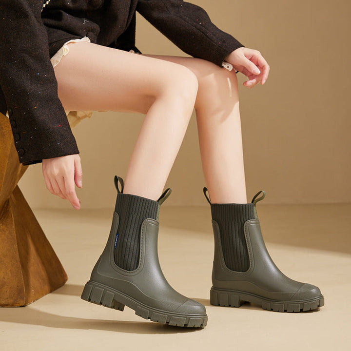 Olive rain boots worn by a seated model in a dark jacket