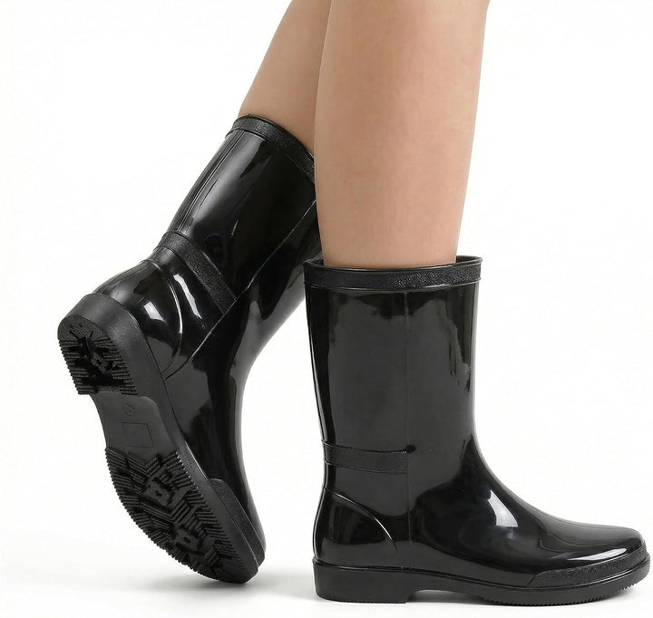 Woman wearing glossy black mid calf rain boots, one foot raised to show the sole